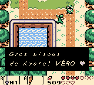 Une capture d’écran du jeu, avec un dialogue « Bon baisers de Kyoto! VÉRO ❤️ » avec un accent sur le E de Véro.